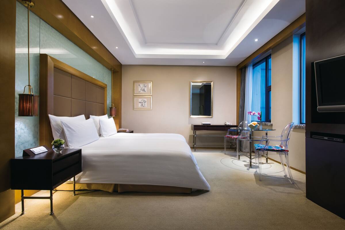 A hotel room with a large bed, a desk with a chair, a TV, and a window with curtains.