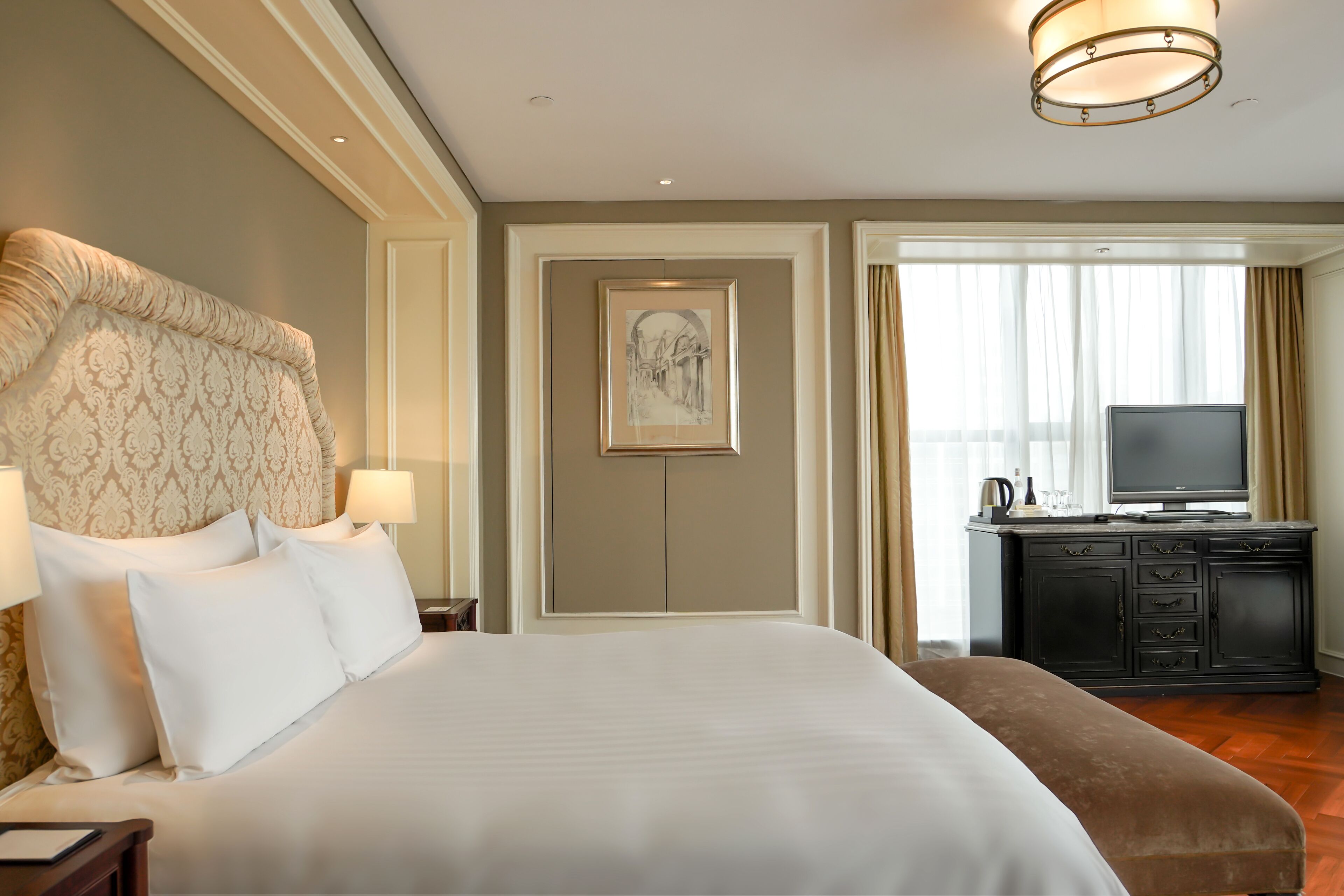 Habitación de hotel con una cama grande, un escritorio con televisor y vistas a la ciudad desde la ventana.
