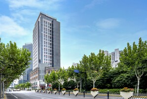Un hotel slanciato dal design moderno, situato in una strada cittadina alberata con cielo sereno.