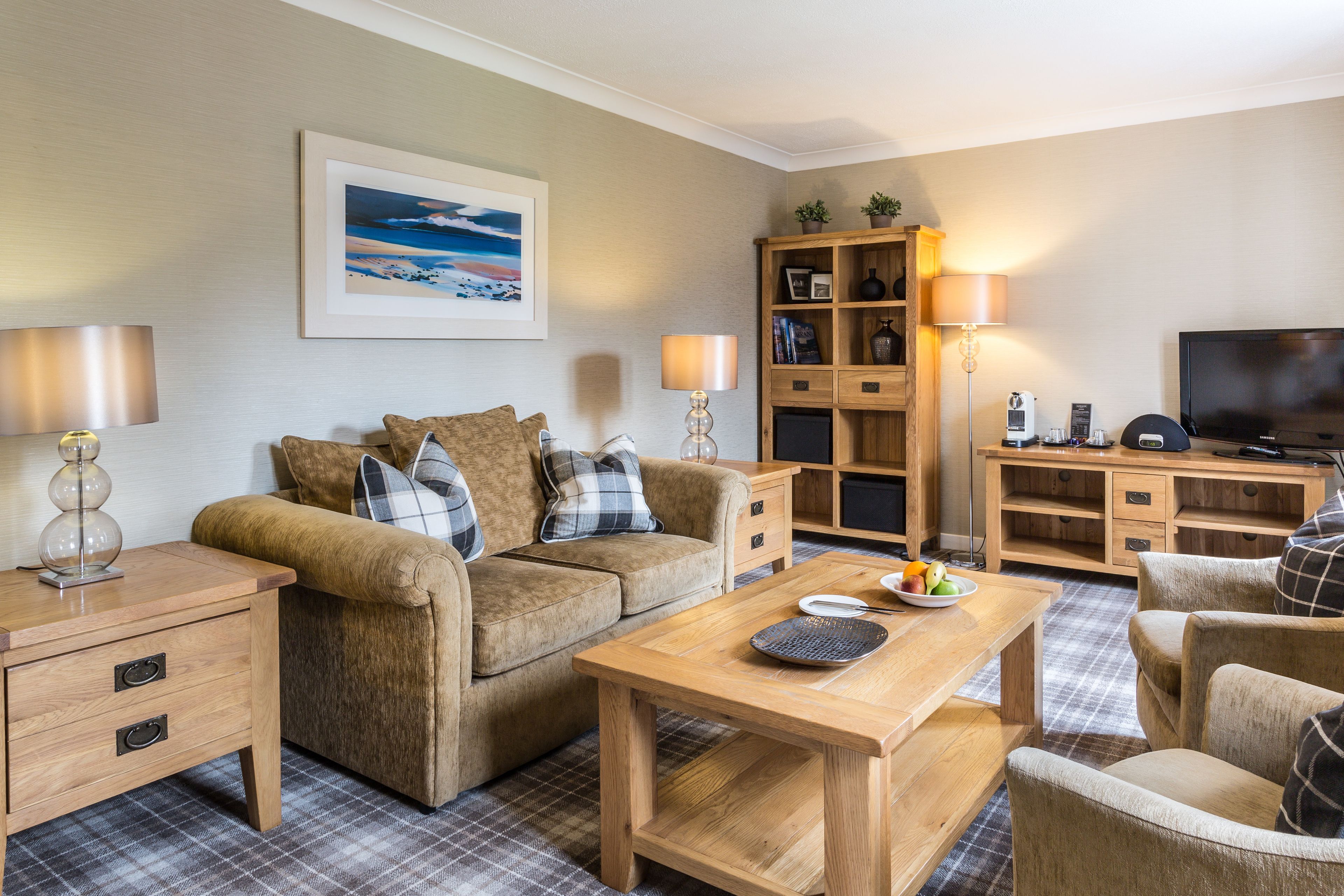 A cozy living room with a sofa, a coffee table, and a TV. There is a bookshelf and a lamp.