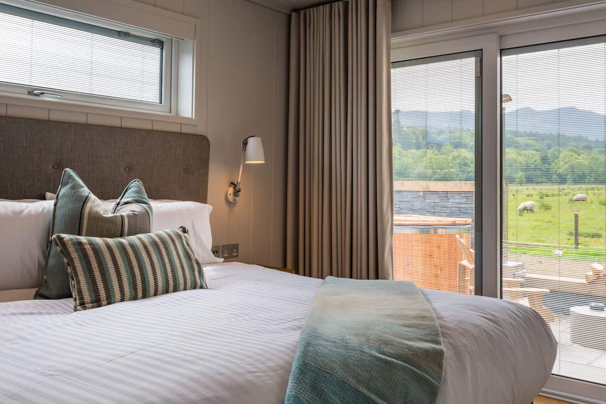A hotel room with a large bed, a view of a green landscape, and a window with blinds.