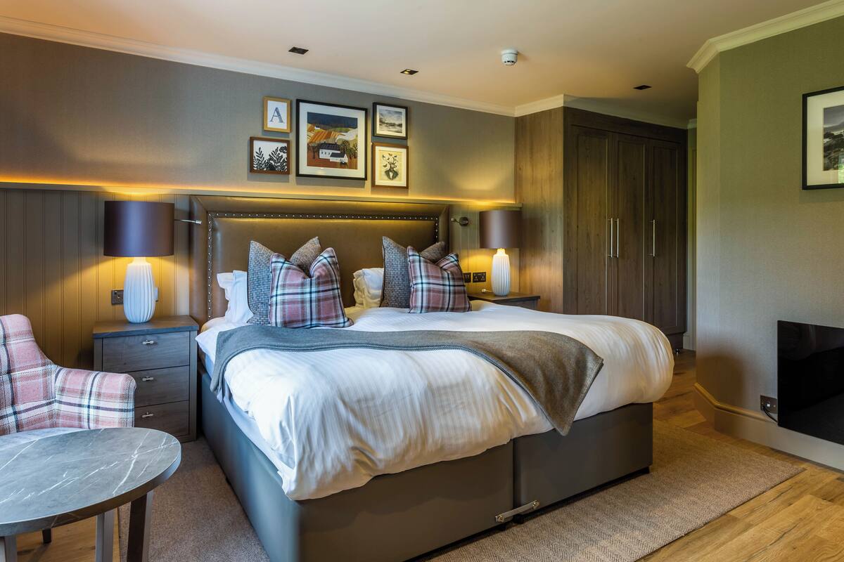 A modern bedroom with a large bed, bedside tables, a chair, and a fireplace.