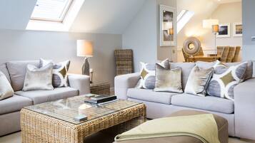 A modern living room with two sofas, a glass coffee table, and a wicker side table.