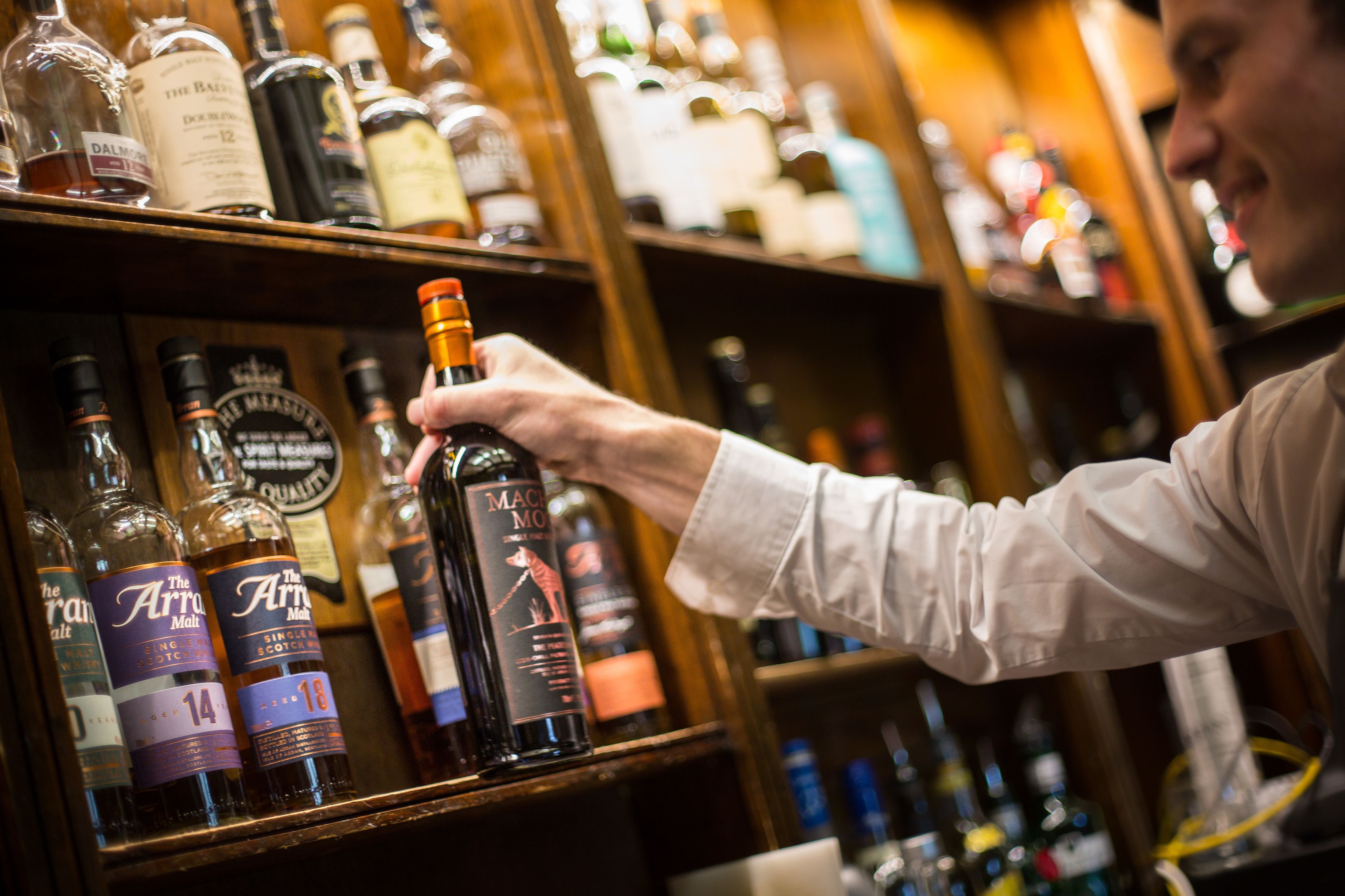 A person selecting a bottle from a shelf stocked with various liquor bottles.