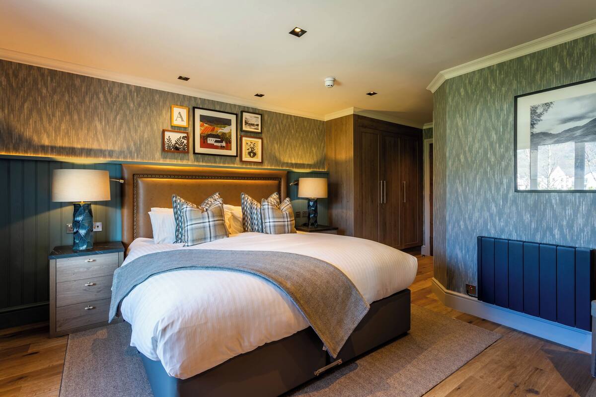 A bedroom with a large bed, two bedside tables with lamps, a headboard, and framed pictures on the wall.