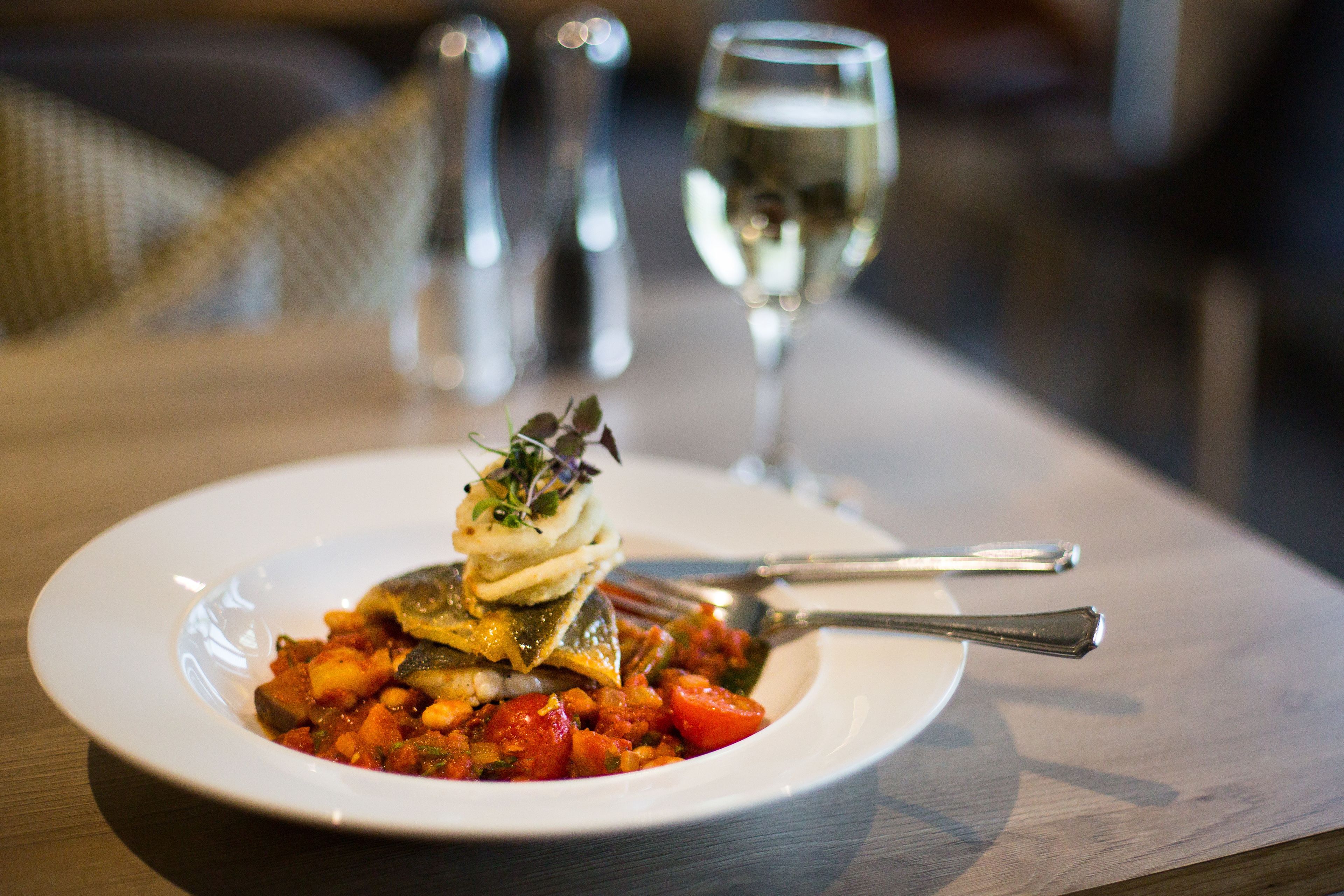 A plate of food with a fork and a glass of white wine on a table.