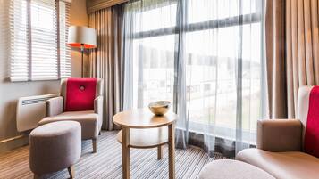 A hotel room with a sofa, armchair, ottoman, and a small table with a bowl.