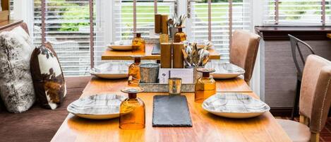 A dining table set with plates, bowls, and glassware, surrounded by chairs and a bench.
