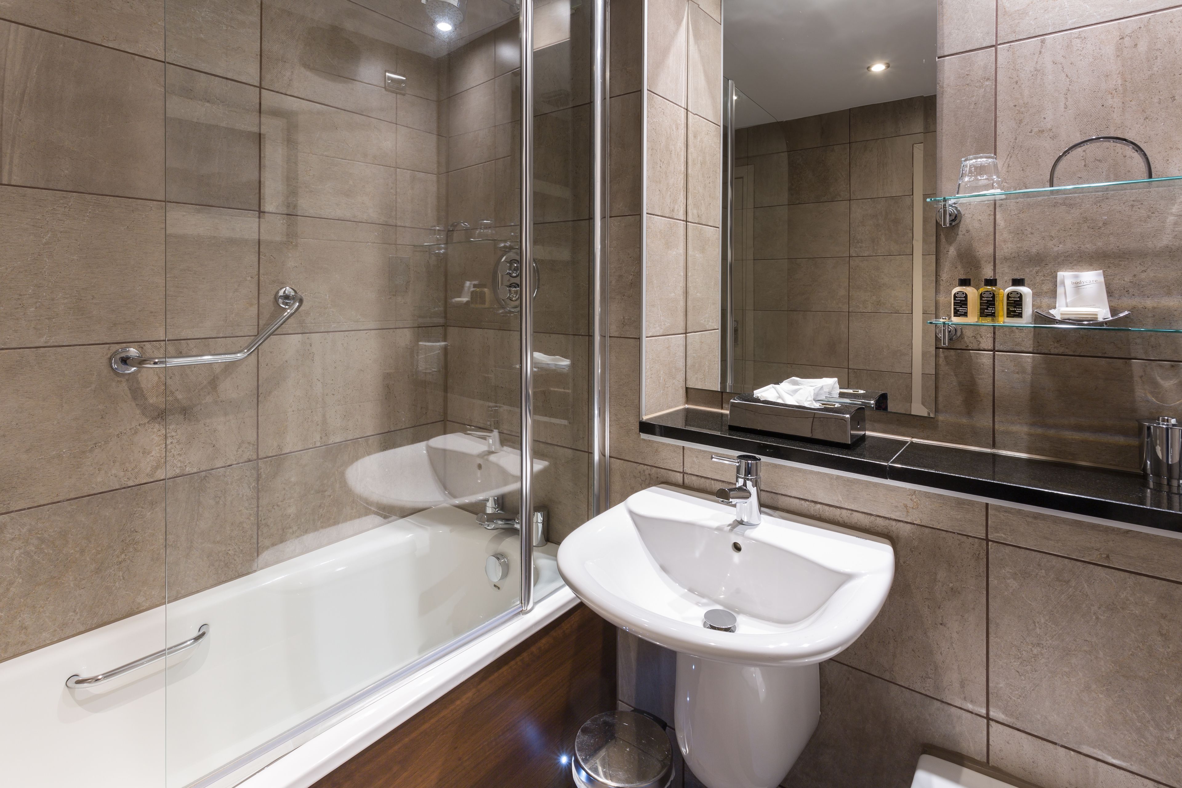 A modern bathroom with a glass-enclosed shower, a white sink, and a large mirror.