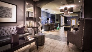 A modern lobby with a sofa, armchair, and ottoman, a reception desk, and a wall with a framed artwork.