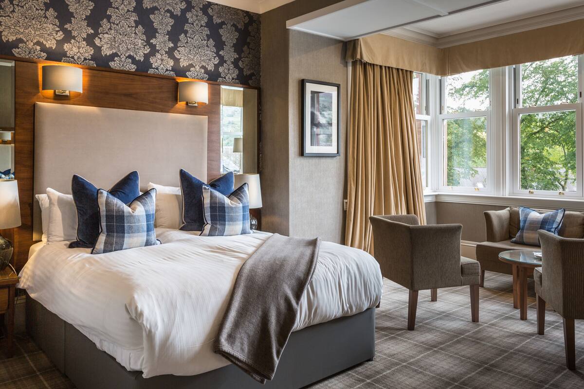 A hotel room with a large bed, two side tables, a sofa, and a window with curtains.