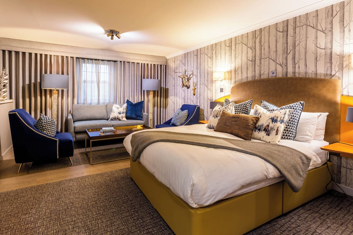 A hotel room with a large bed, two armchairs, a sofa, a coffee table, and a lamp.