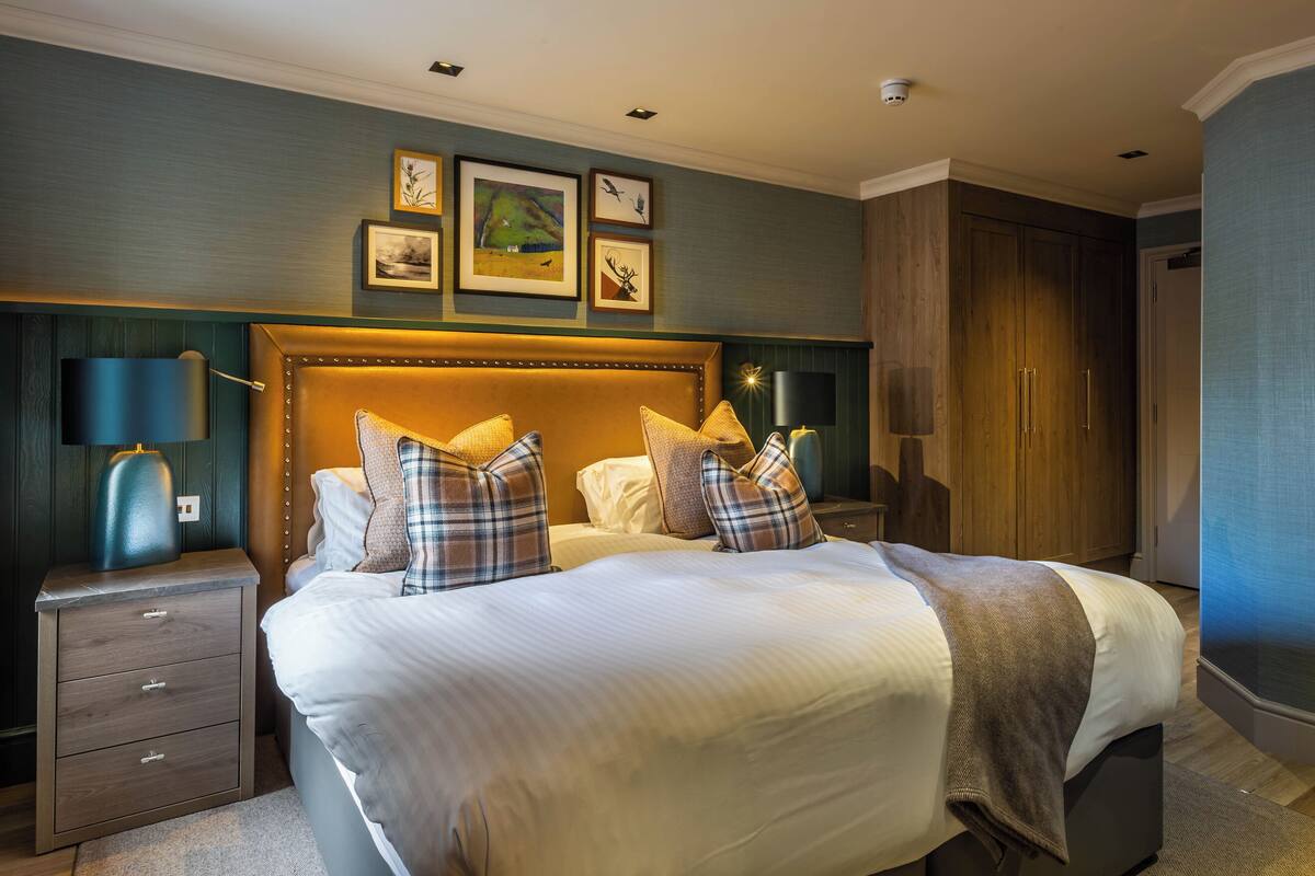 A hotel room with a large bed, two bedside tables, a headboard with a built-in TV, and framed artwork on the wall.