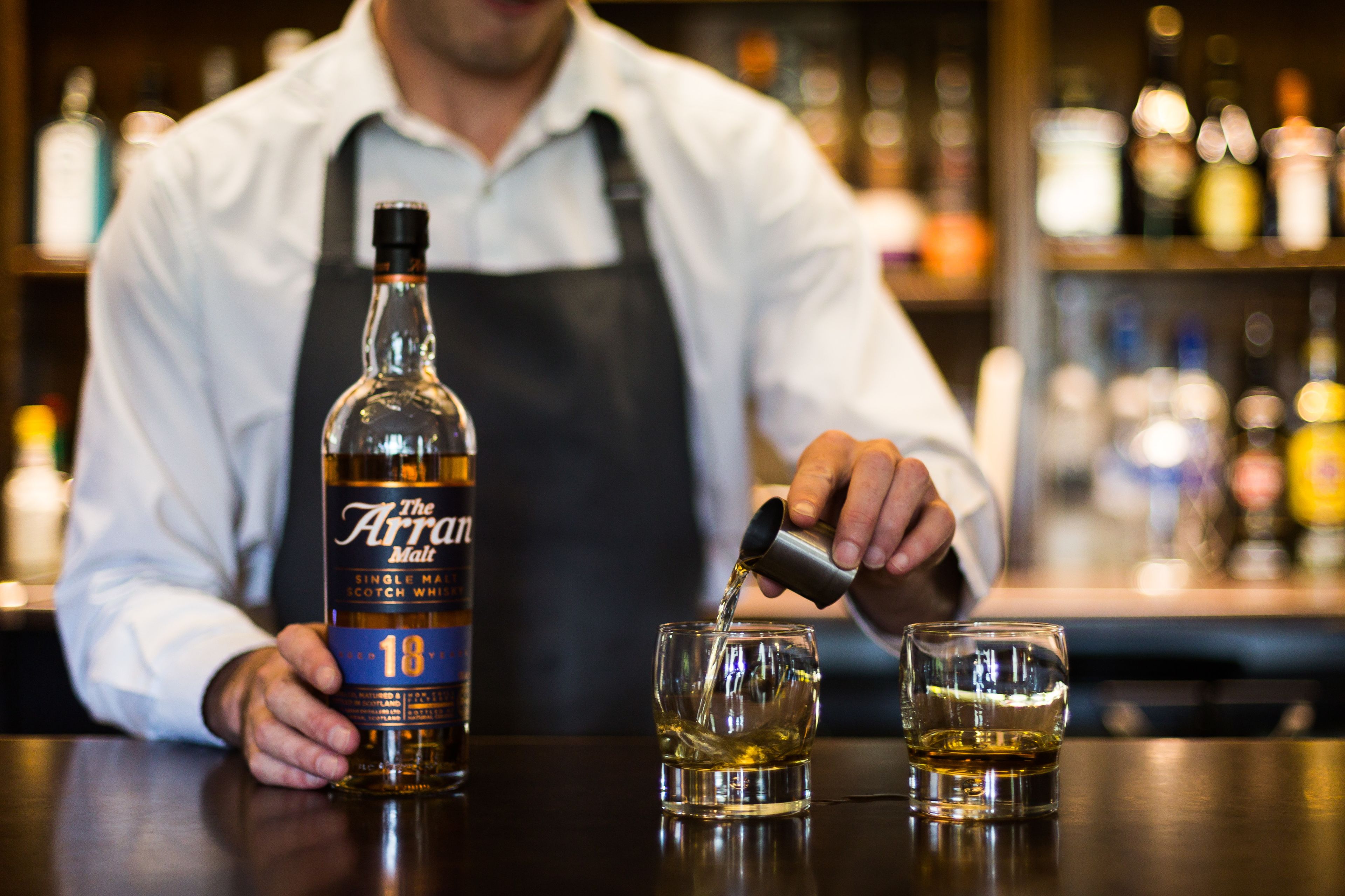 Ein Barkeeper gießt einen Drink aus einer mit 'The Arran Malt' beschrifteten Flasche in ein Glas.