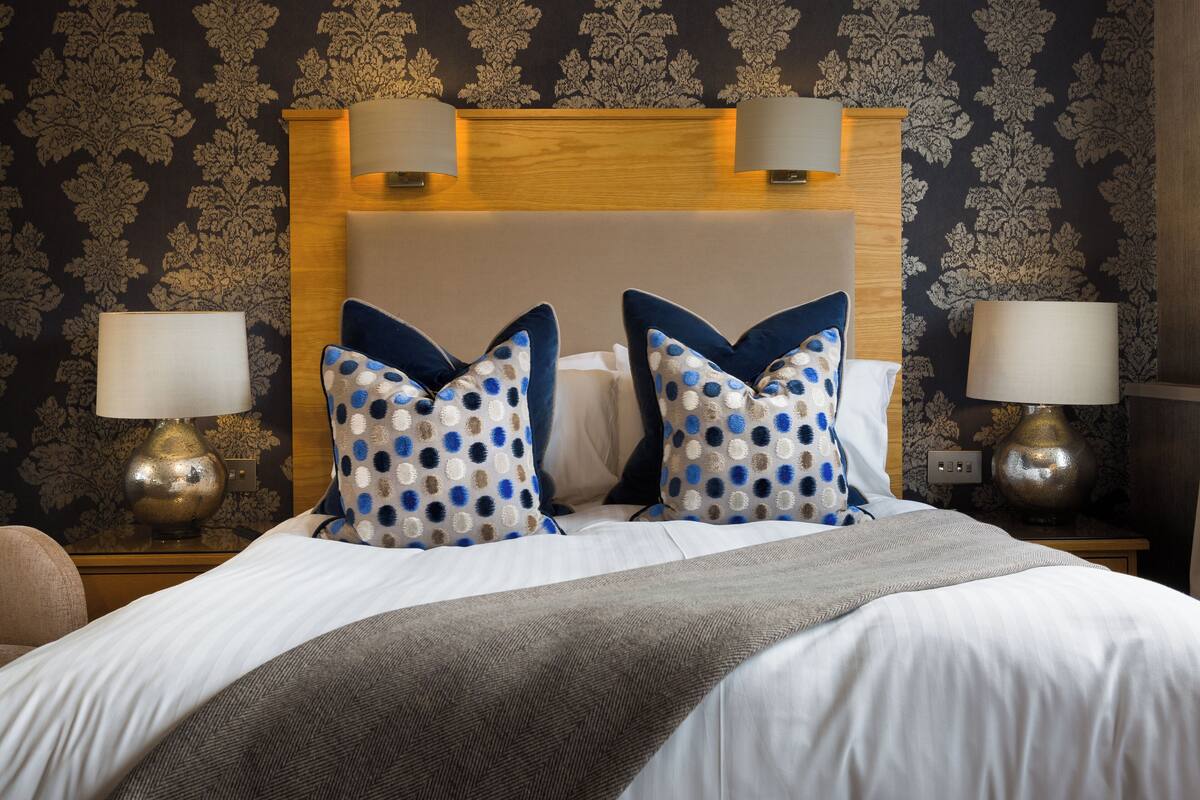 A neatly made bed with a patterned headboard, two bedside lamps, and a patterned wall.