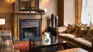 A cozy living room with a fireplace, plaid furniture, and a large mirror above it.