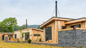 A modern wooden cabin with stone walls, large windows, and a chimney.