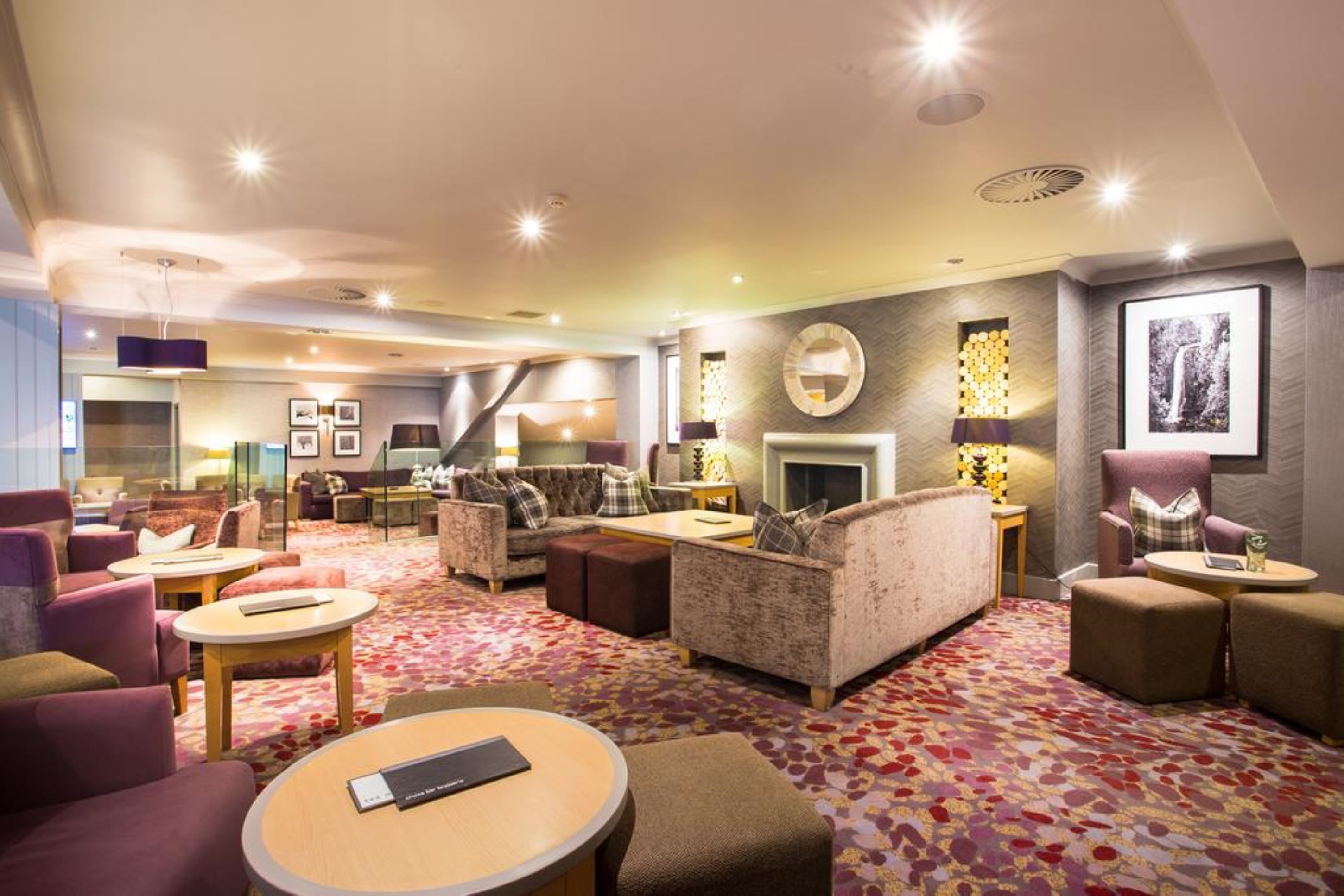 Een hotel lobby met een open haard, comfortabele zithoek en een kamerbreed tapijt.