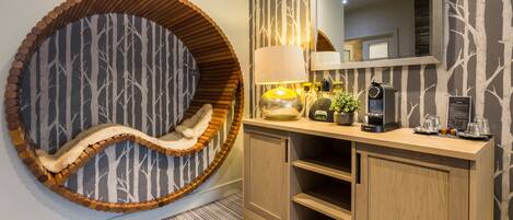 A modern bathroom with a circular wooden bench, a mirror, a coffee machine, and a small plant.
