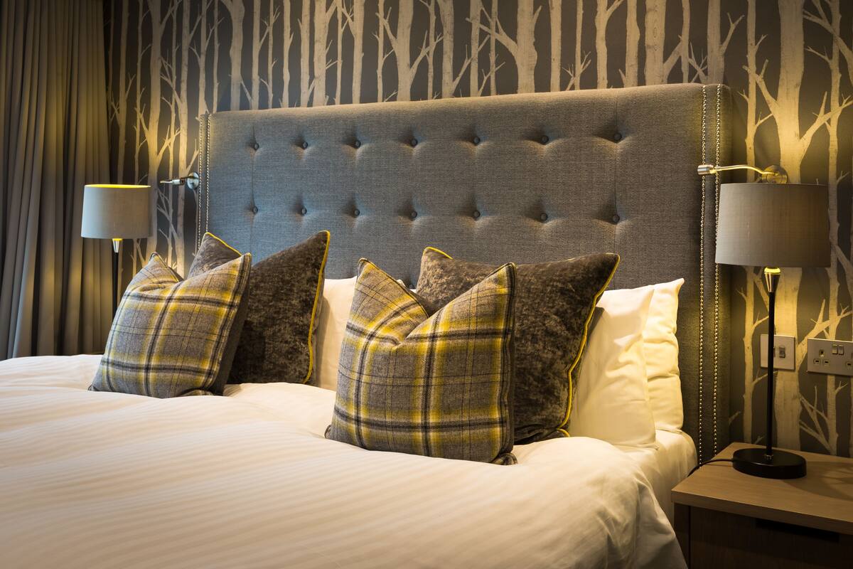 A neatly made bed with plaid pillows, a tufted headboard, and bedside lamps.