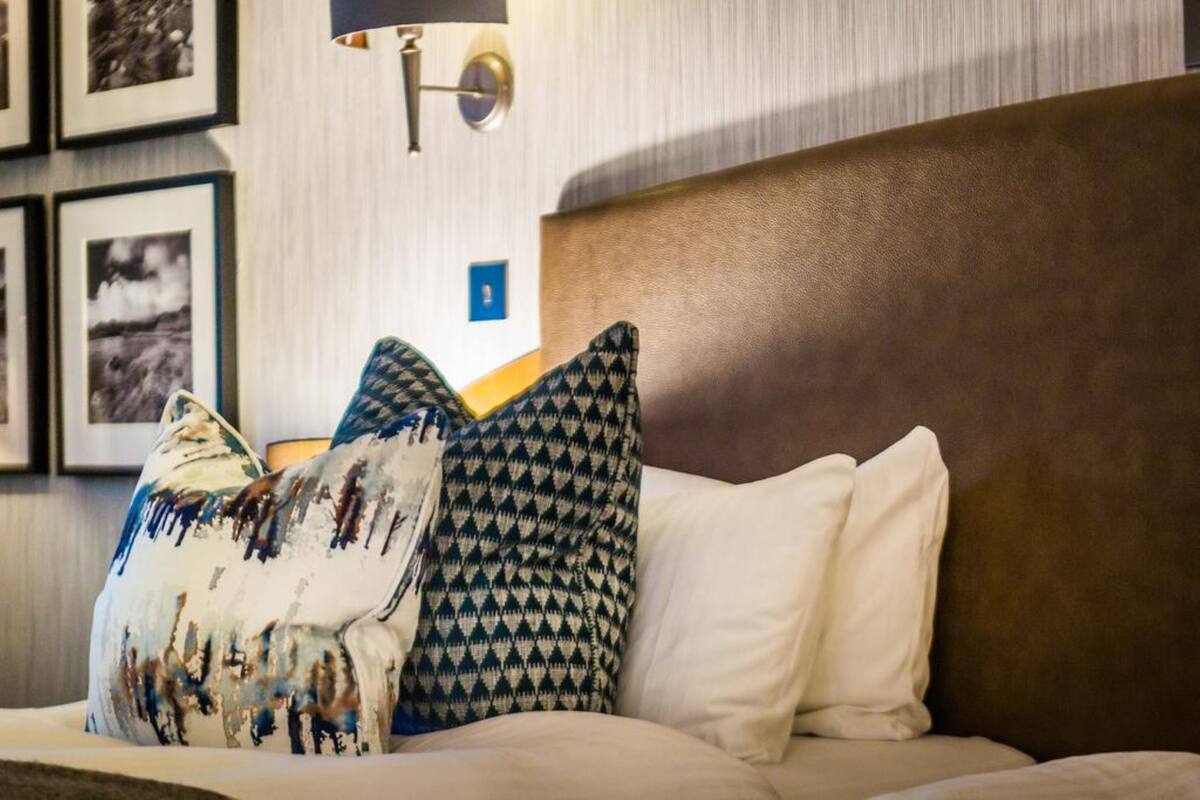 A neatly made bed with patterned pillows and a wall-mounted lamp.