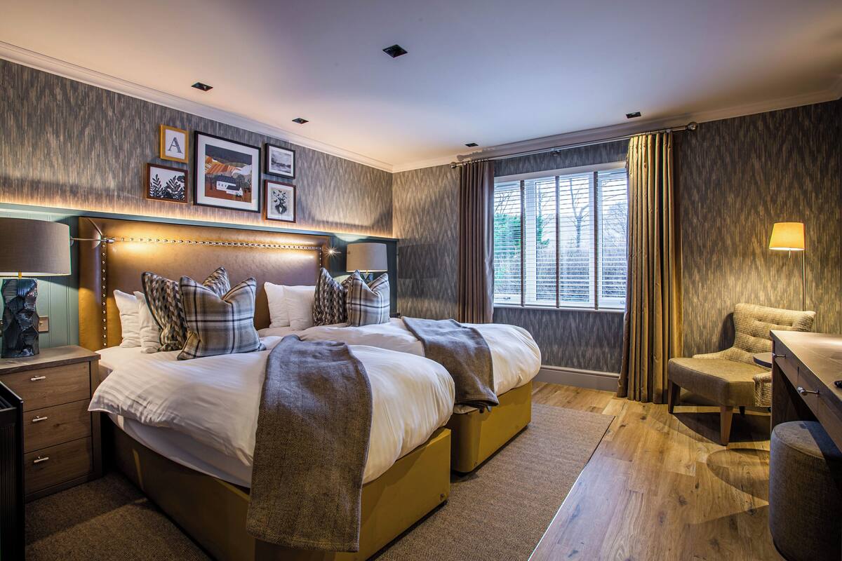 A modern hotel room with a large bed, bedside tables, a desk, and a window with curtains.