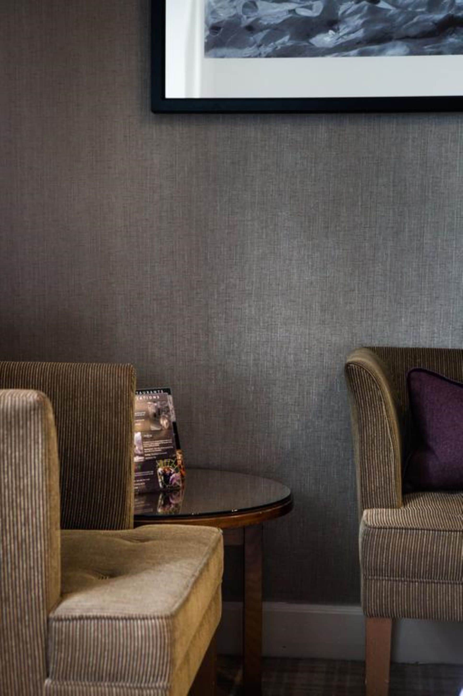 A room with two upholstered chairs, a small round table, and a framed picture on the wall.