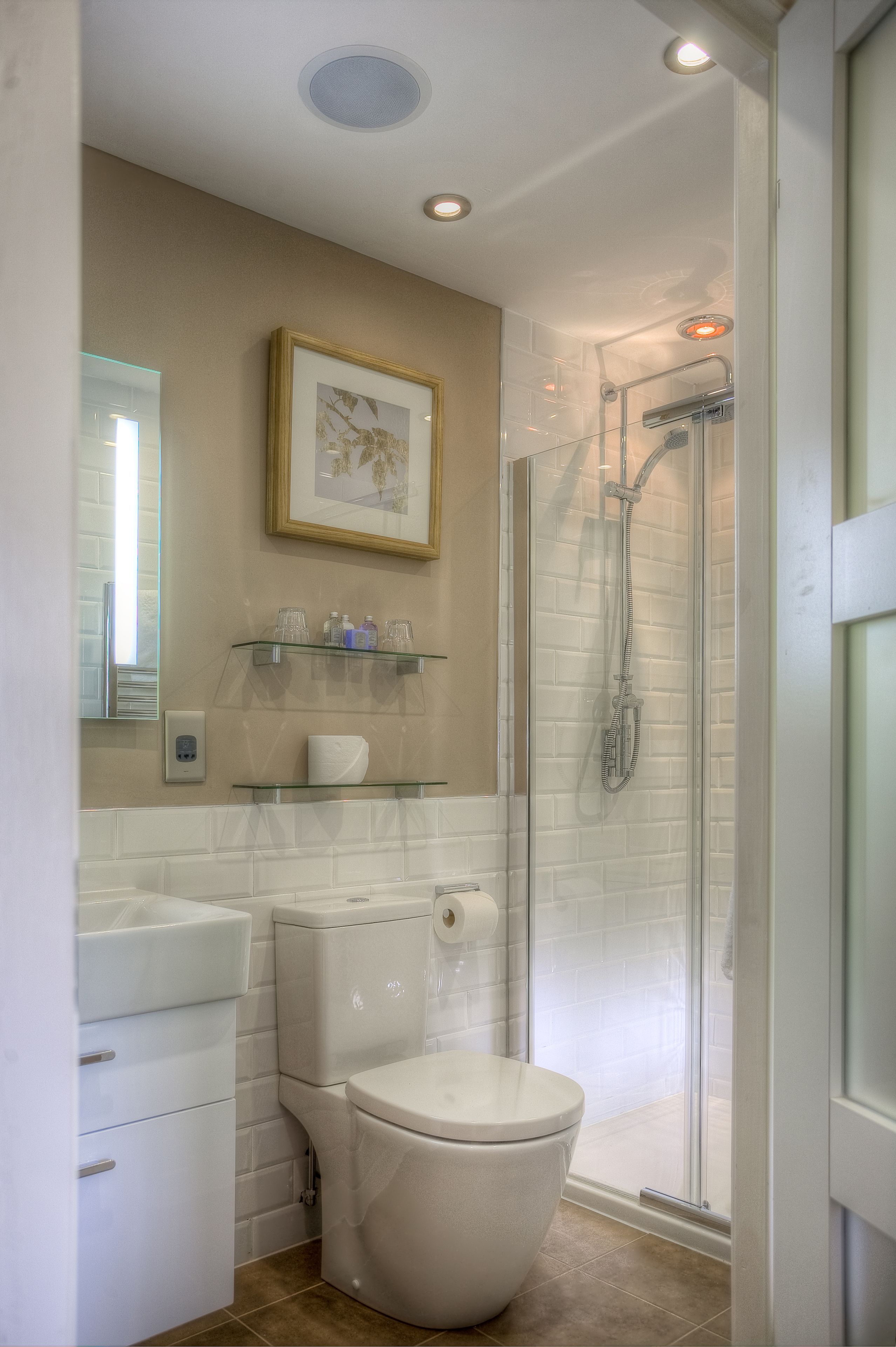 Un baño con inodoro, cabina de ducha de vidrio, lavabo con espejo y un cuadro enmarcado en la pared.