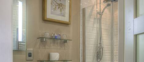 Un baño con inodoro, cabina de ducha de vidrio, lavabo con espejo y un cuadro enmarcado en la pared.