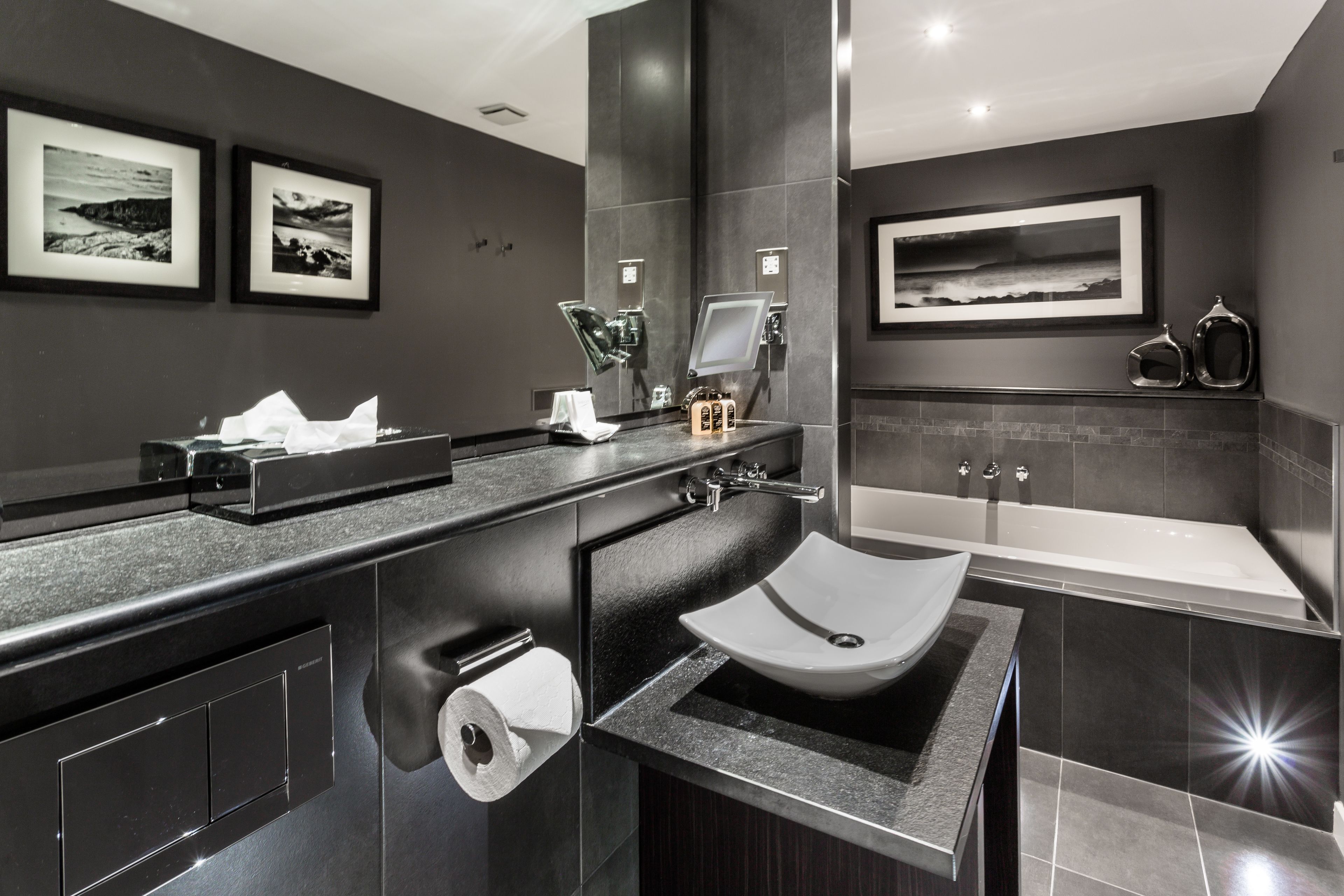 A modern bathroom with a black countertop, a white sink, a large mirror, and a framed picture on the wall.