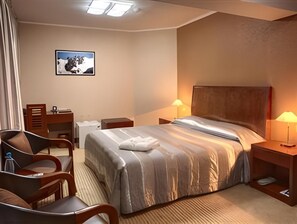A hotel room with a bed, a desk, a chair, and a nightstand with a lamp. - Hotel Voyage (Almaty)