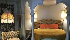A bedroom with a tufted headboard, a four-poster bed, a chaise lounge, and a wall-mounted lamp. - Relax Inn Altoona (Altoona)