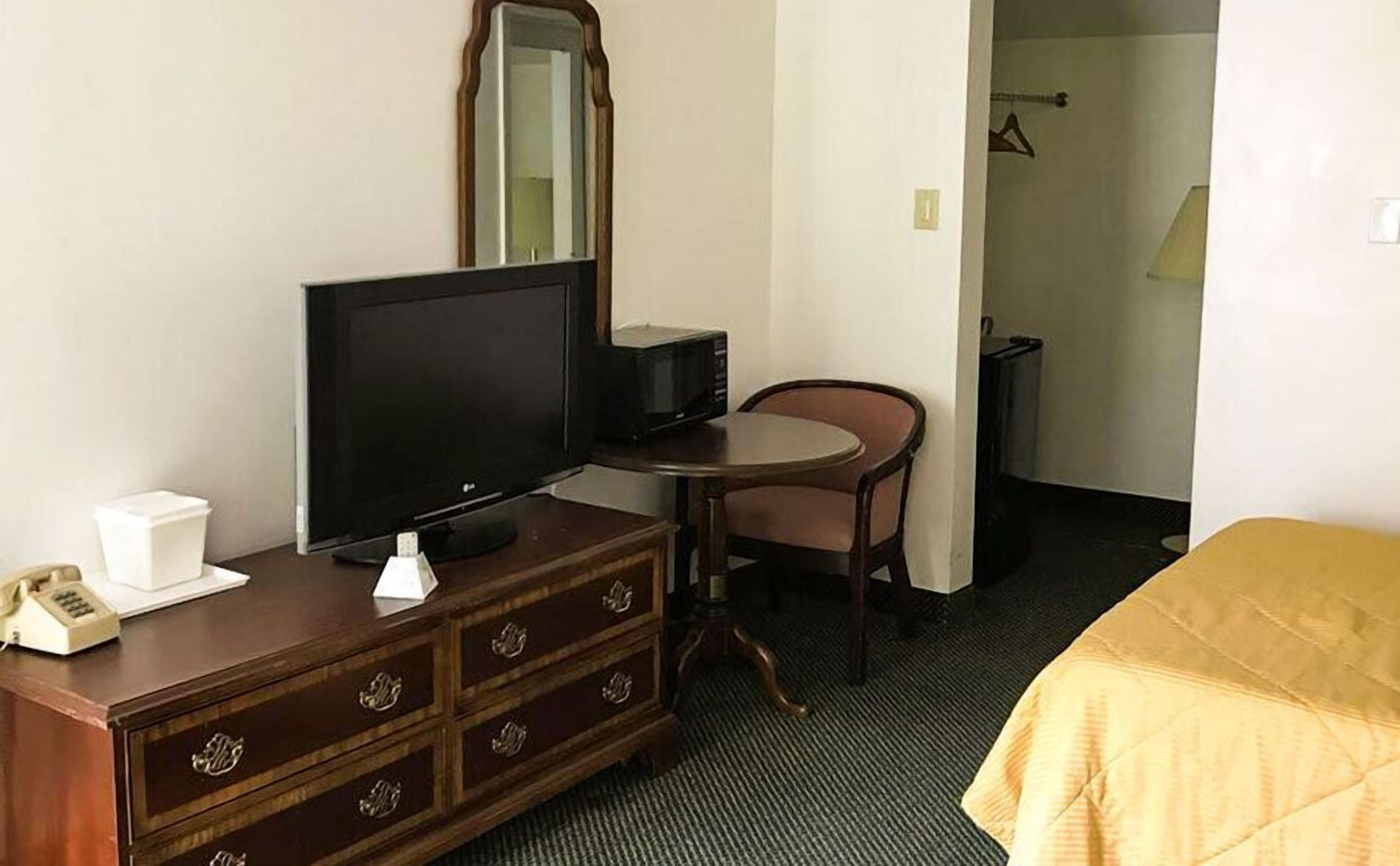 Habitación de hotel con televisión, una mesita, una silla, cómoda y cama.