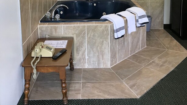 A bathroom with a large bathtub, a mounted television, and a telephone on a small table. - Relax Inn Altoona (Altoona)