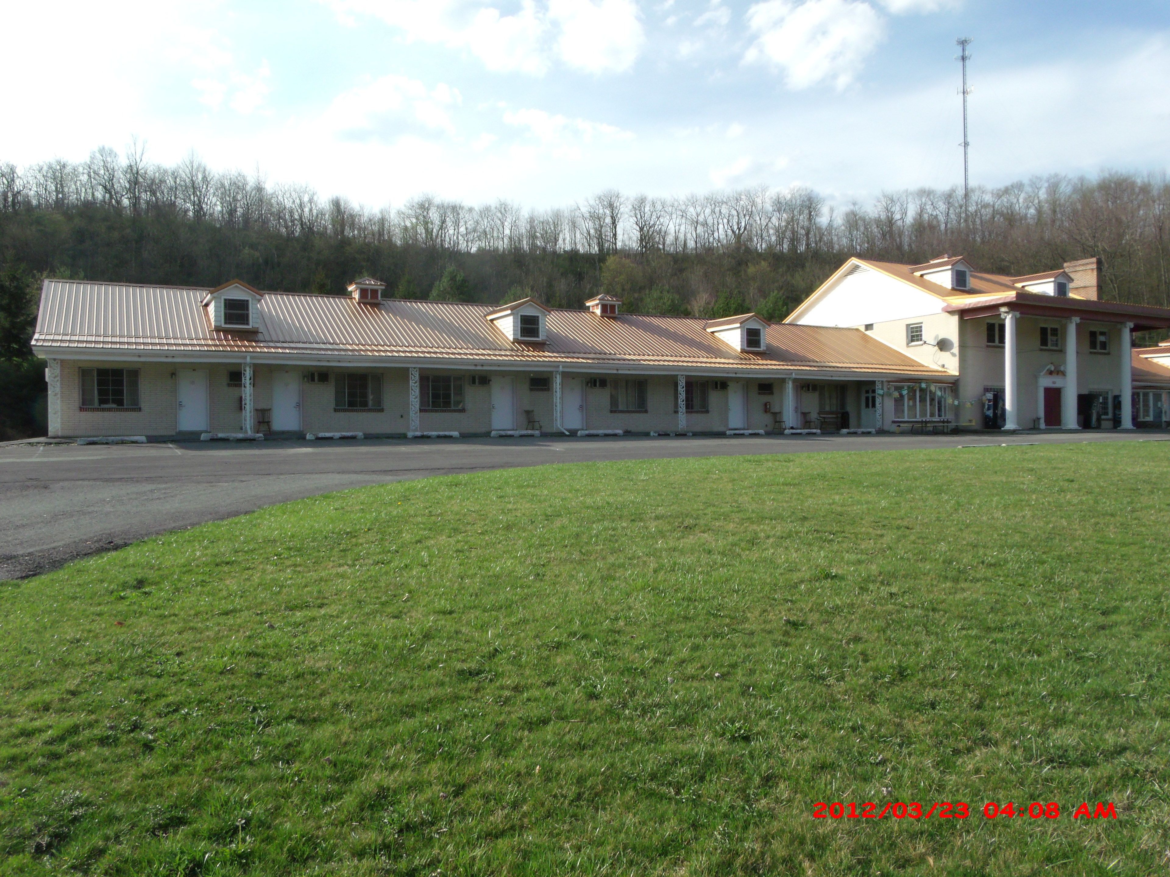 Un motel con un edificio de una sola planta y varias habitaciones, junto a un estacionamiento.