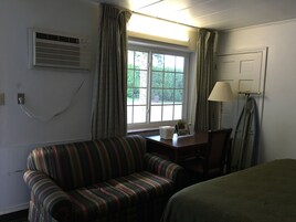 Una habitación con un sofá a rayas, una mesita con una lámpara, una ventana con cortinas y un equipo de aire acondicionado en la pared.