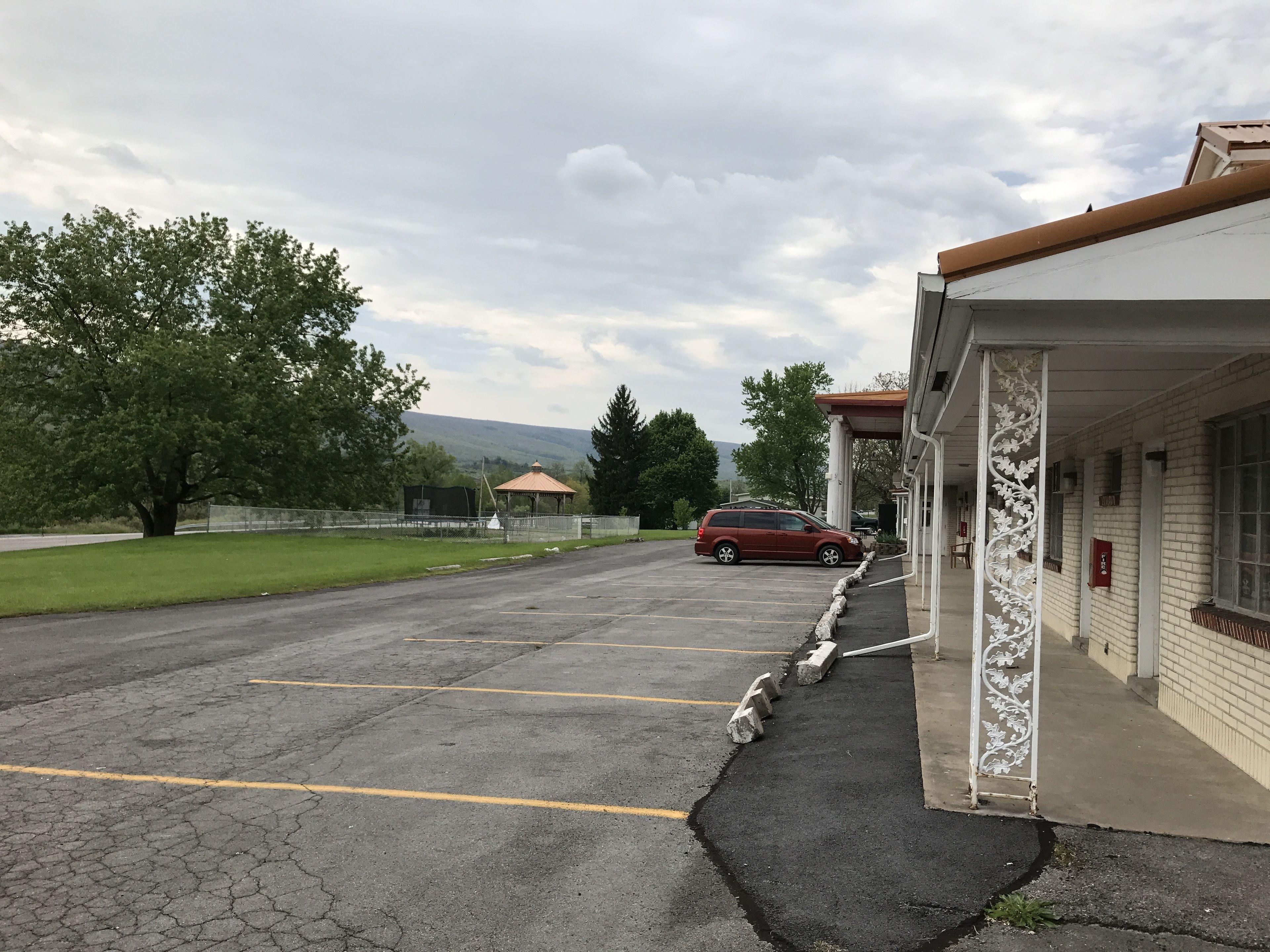 Un parking avec une voiture rouge, un kiosque et un bâtiment à la façade en briques.
