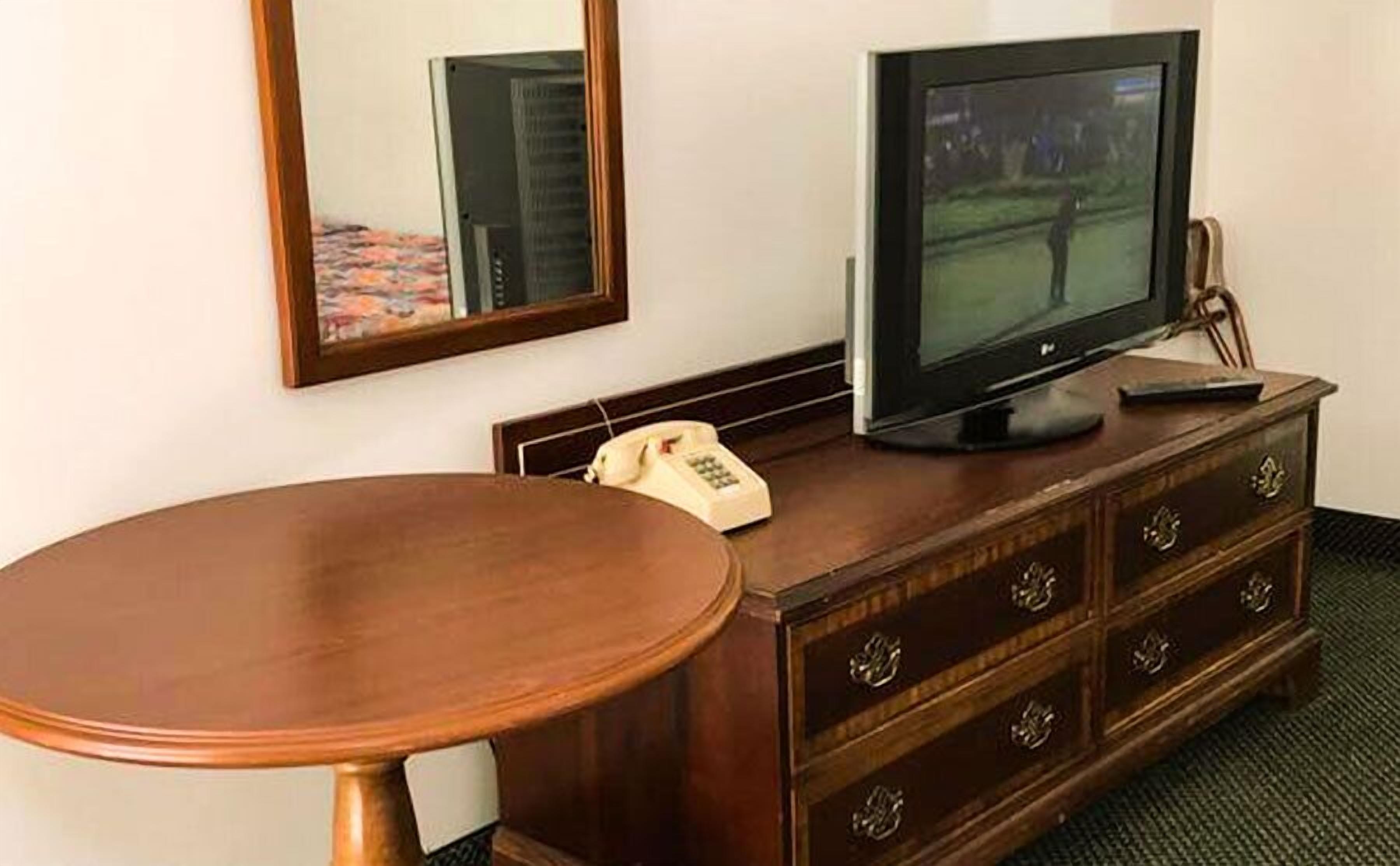 Uma cômoda de madeira com uma televisão, um telefone e um espelho.