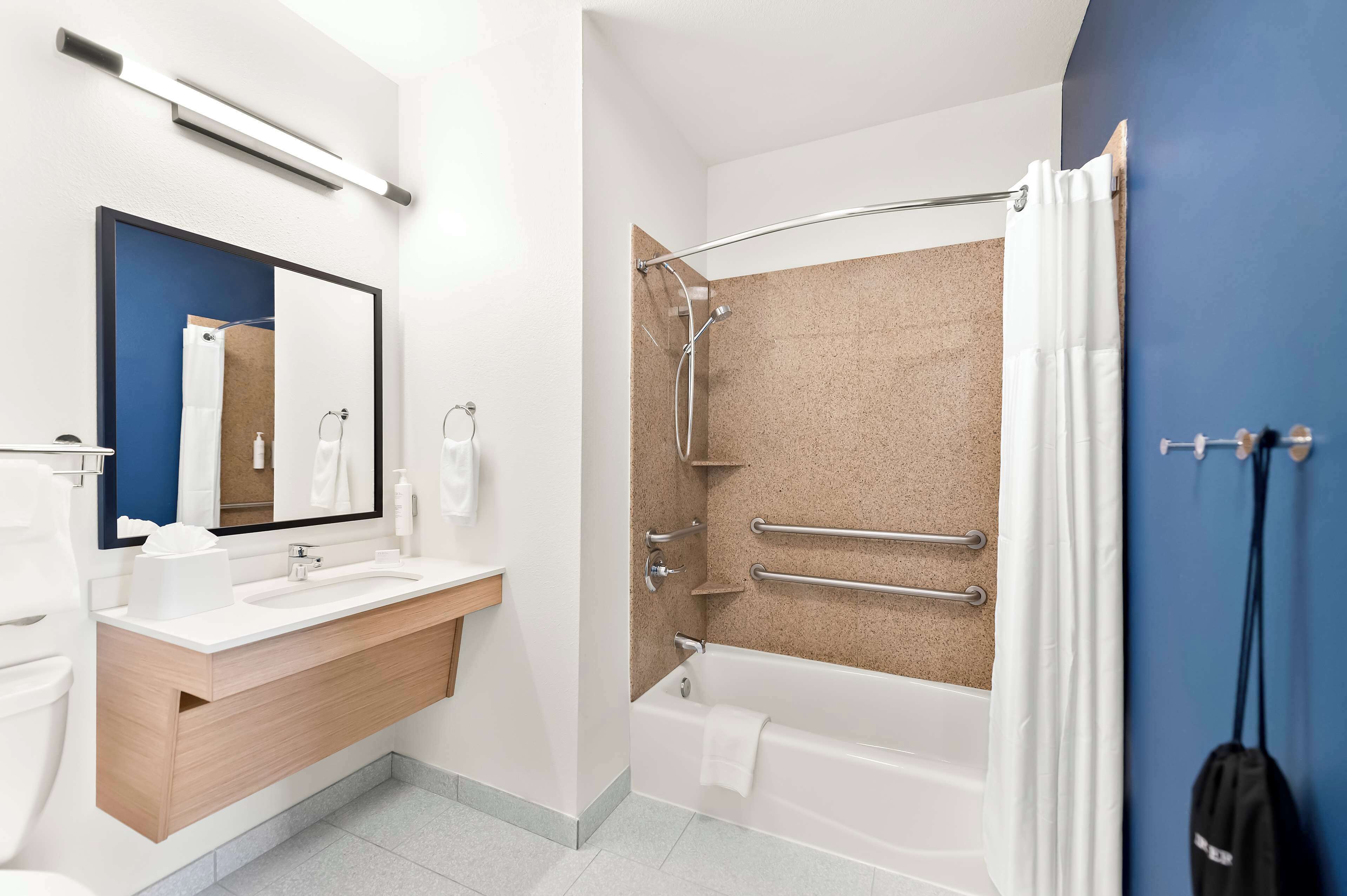 Un baño moderno con un lavamanos, espejo y bañera blancos.