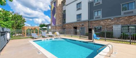 A hotel with a swimming pool, outdoor seating, and a stone facade.