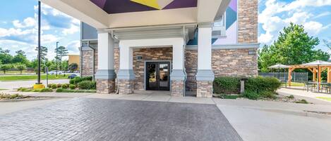 A building entrance with a stone facade, a covered walkway, and outdoor seating area.