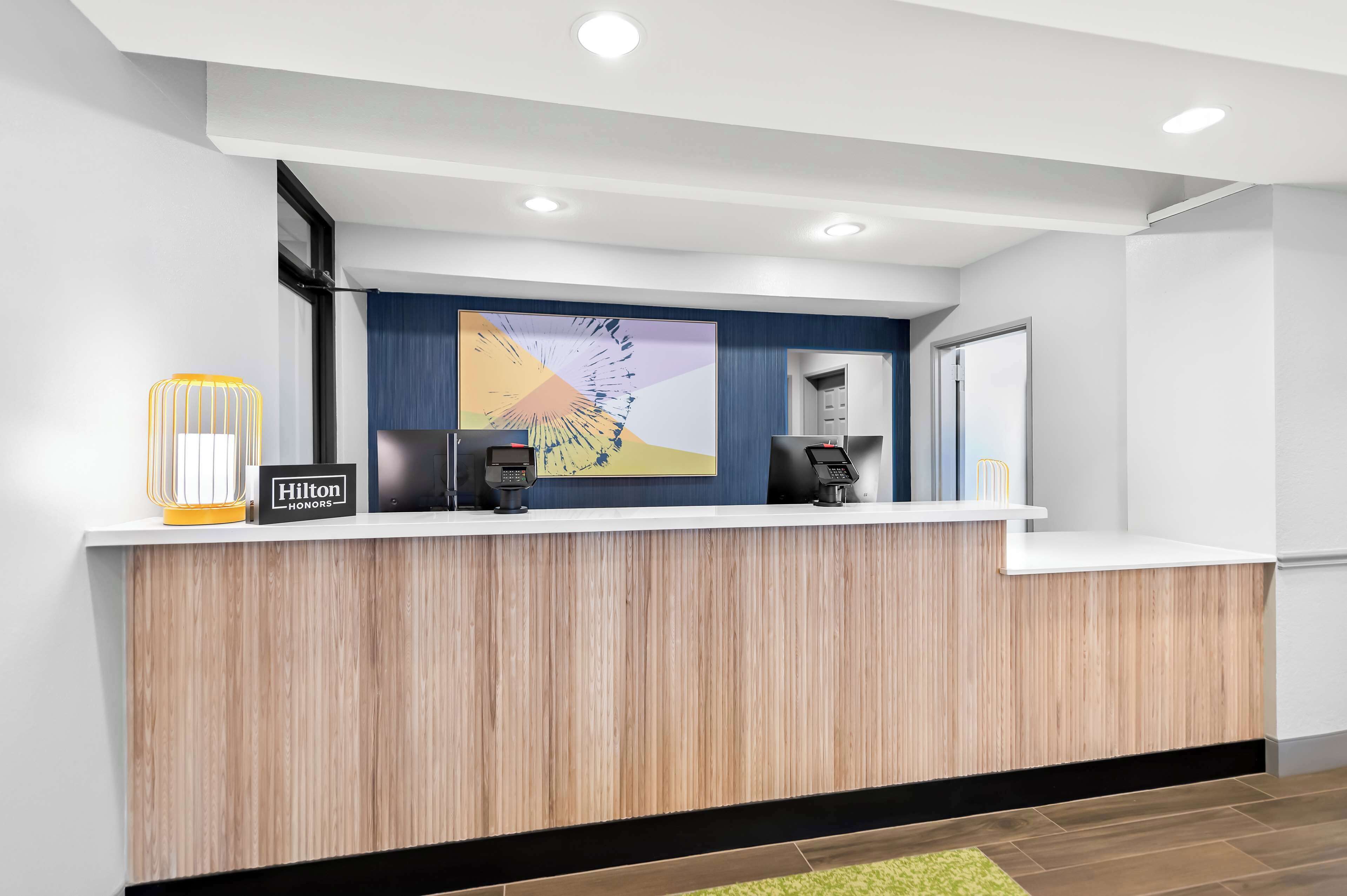A modern hotel reception desk with a wooden finish, a large abstract painting, and a 'Hilton Honors' sign.