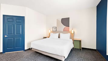 Ein Hotelzimmer mit einem großen Bett, einer blauen Tür, einem Nachttisch mit Lampe und einem an der Wand hängenden Kunstwerk.