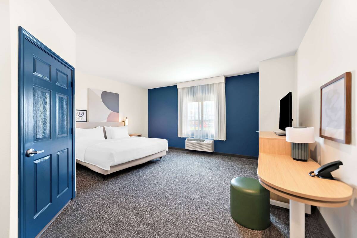A hotel room with a bed, a desk, a chair, a TV, and a window with curtains.