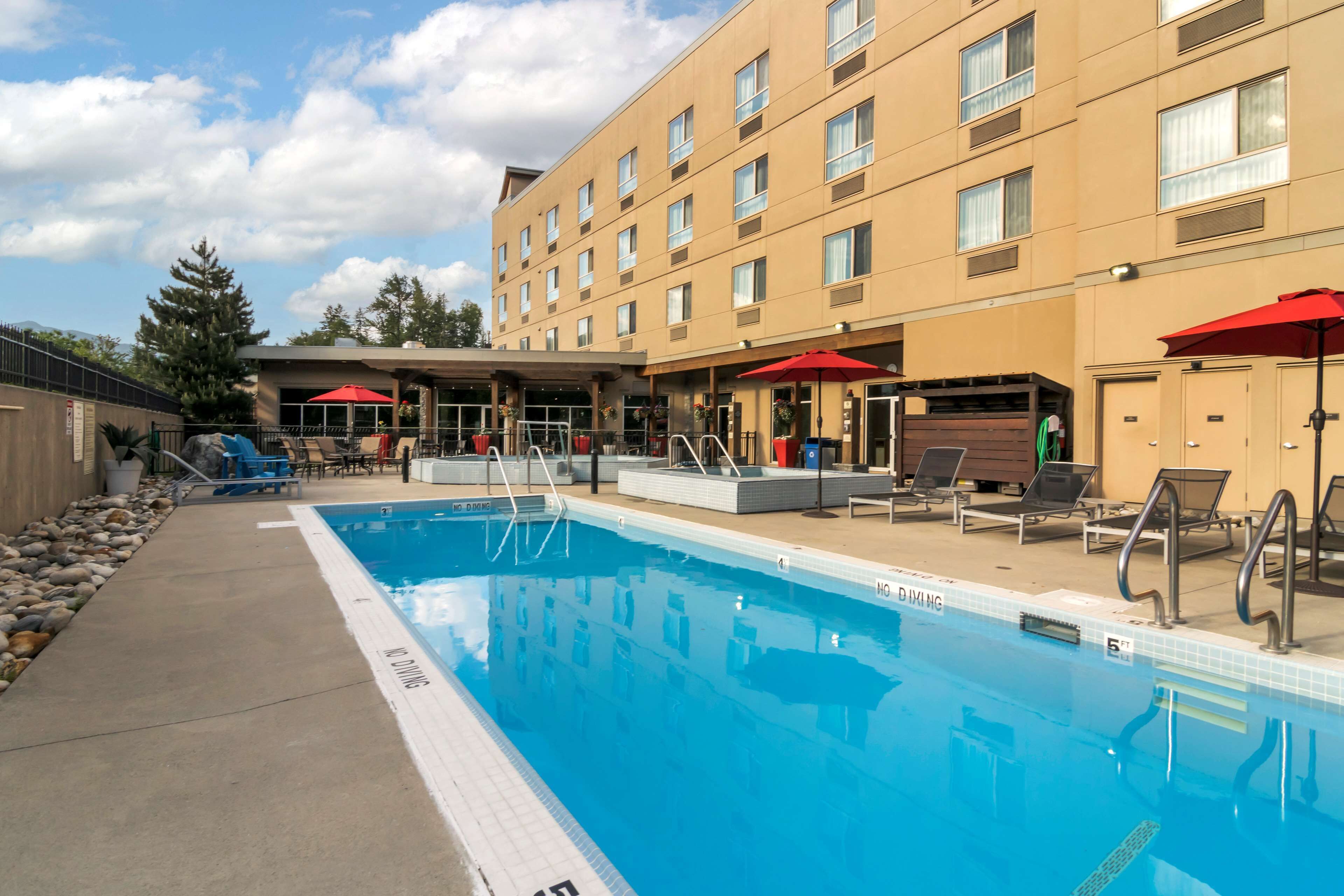 A hotel pool area with a clear blue pool, sun loungers, and umbrellas.