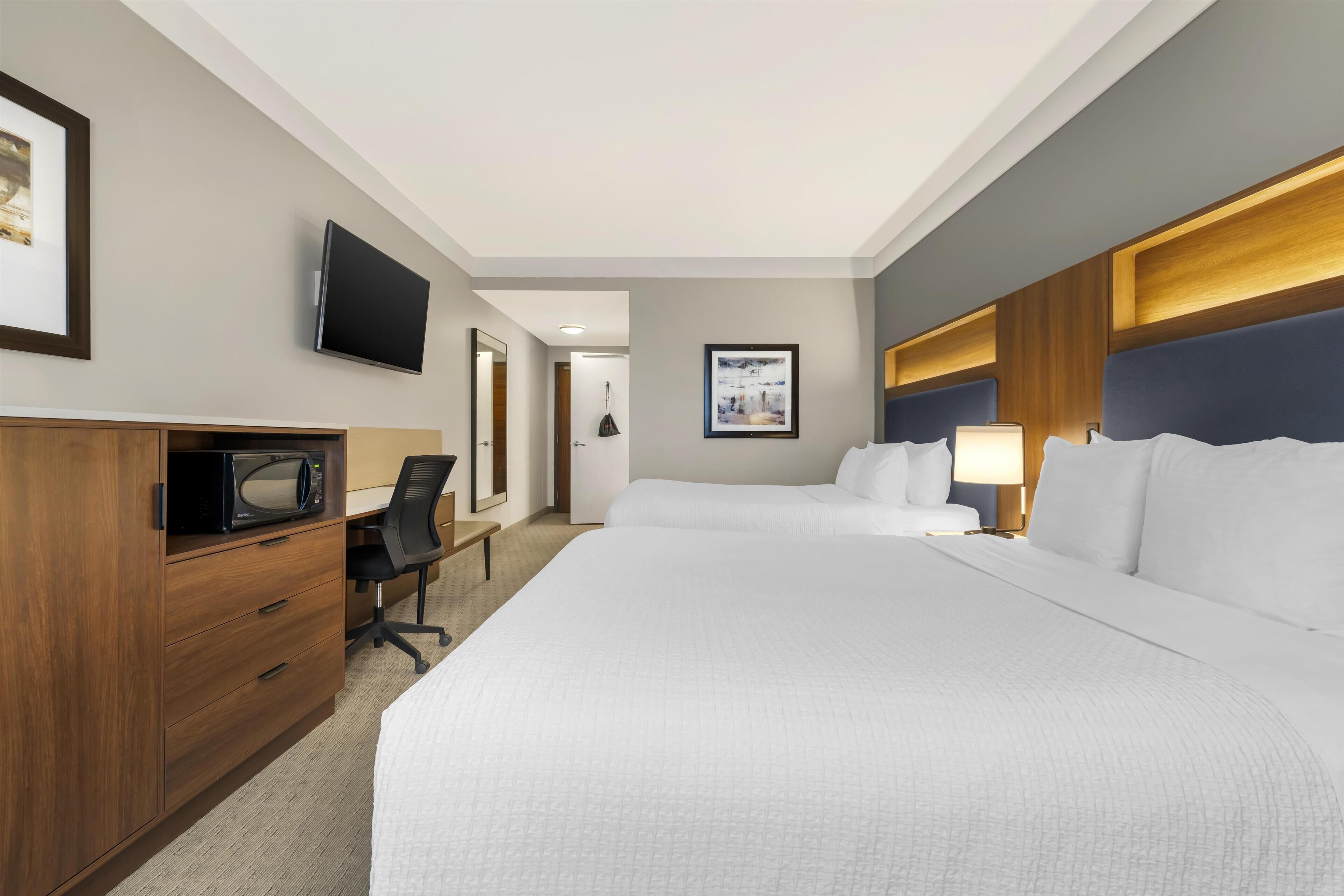 A hotel room with a large bed, a desk with a chair, a television, and a framed picture on the wall.