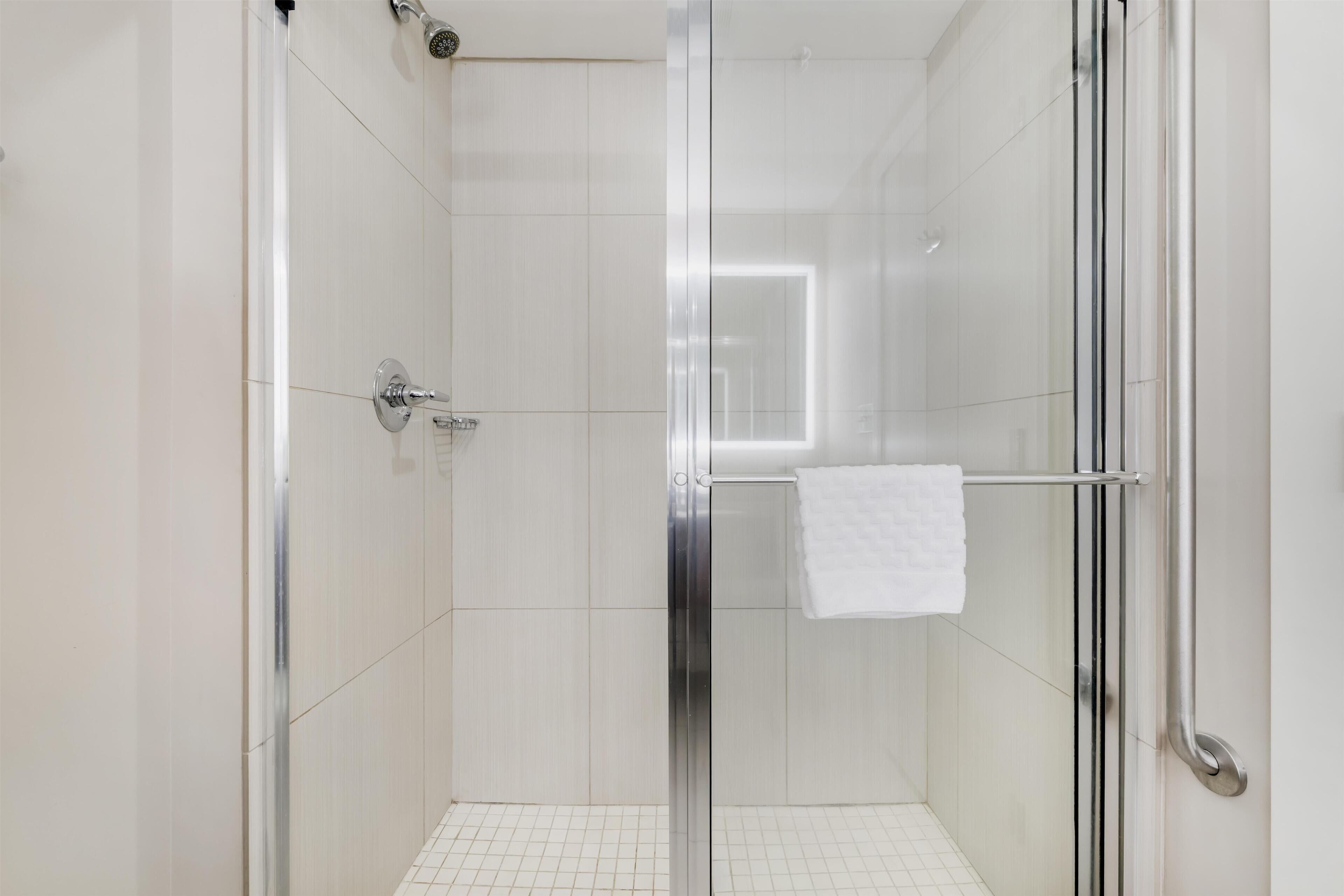 A modern shower with a glass door, white tiles, and a towel rack.