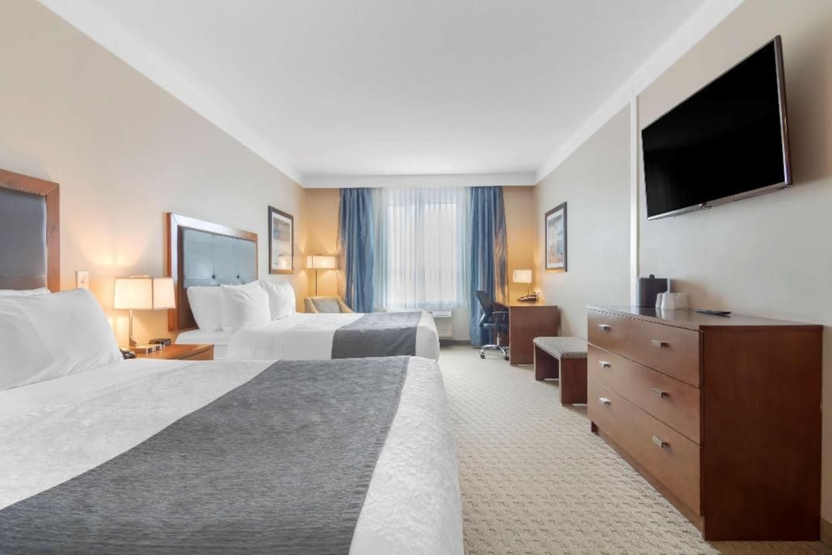 A hotel room with two beds, a desk, a chair, a dresser, and a TV.