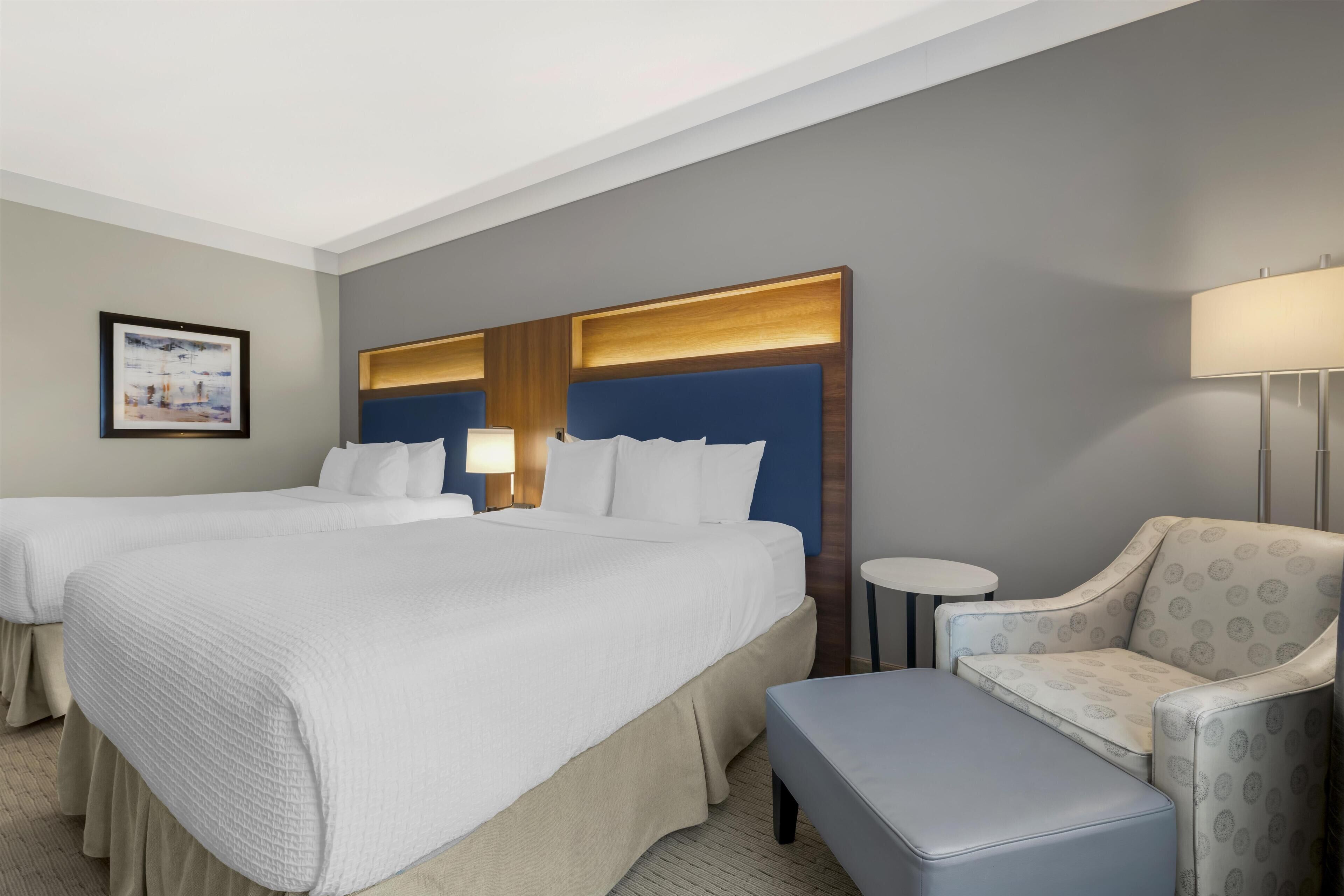 A hotel room with two beds, a small round table, a chair, and a bench.