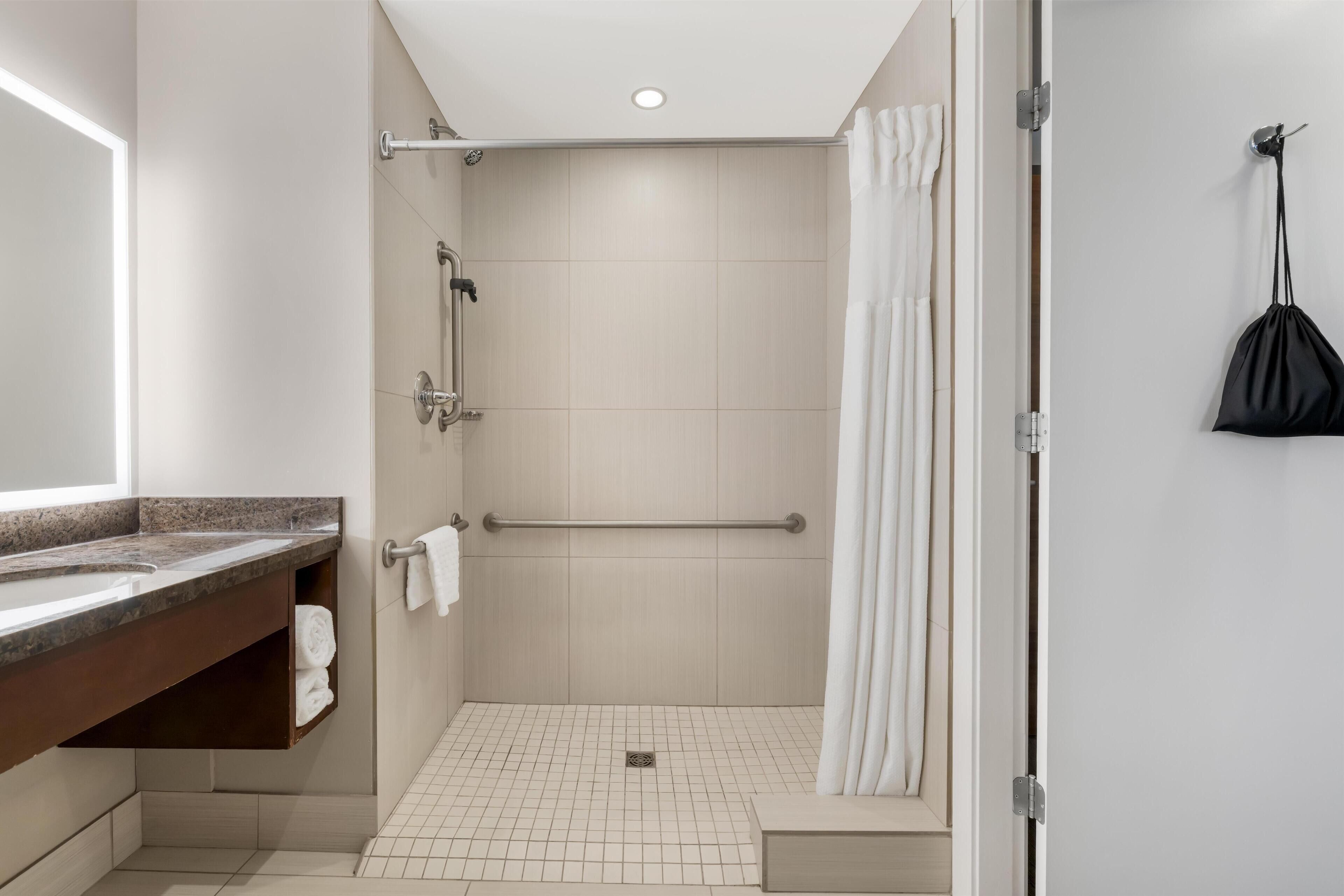A modern bathroom with a shower, a sink with a towel rack, and a hanging bag.